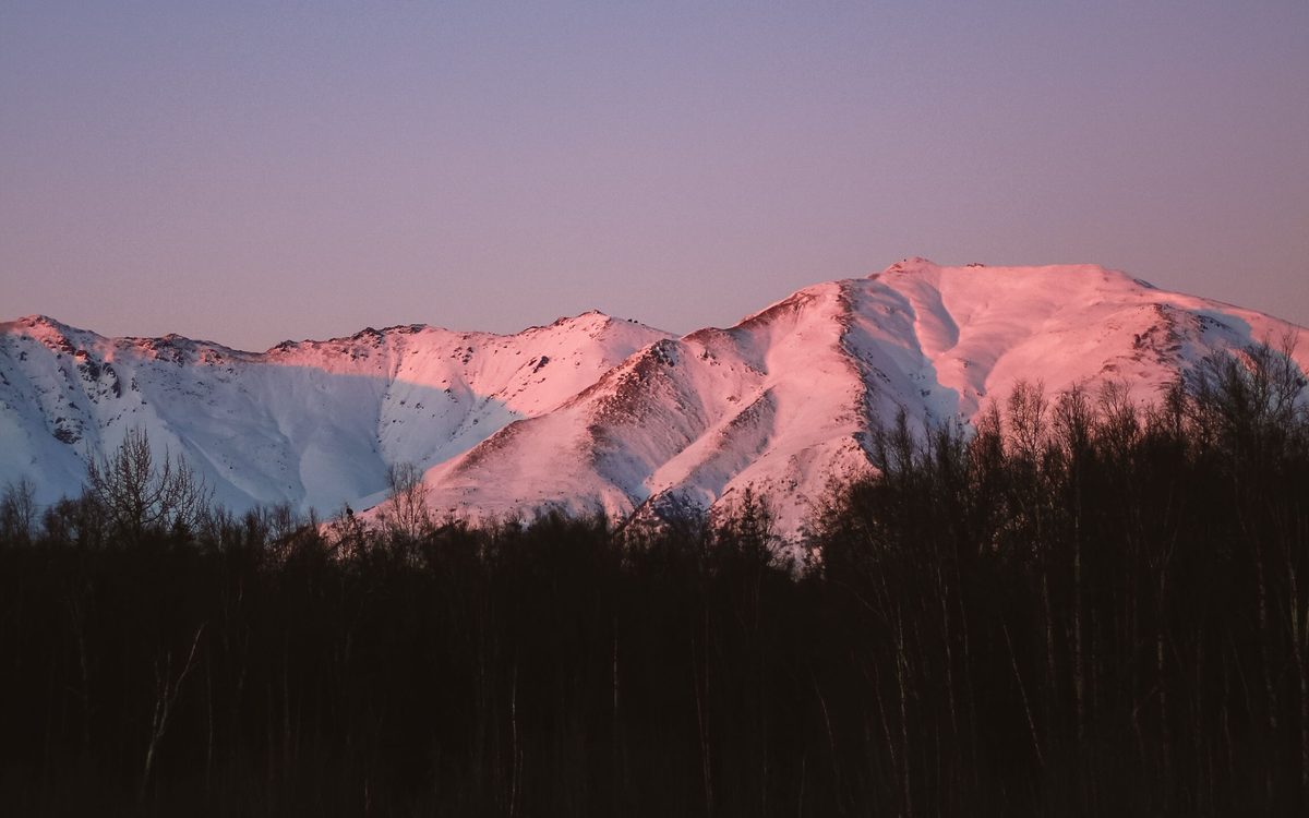 Alpenglow on snow-covered peaks above a frozen lake, Alaska