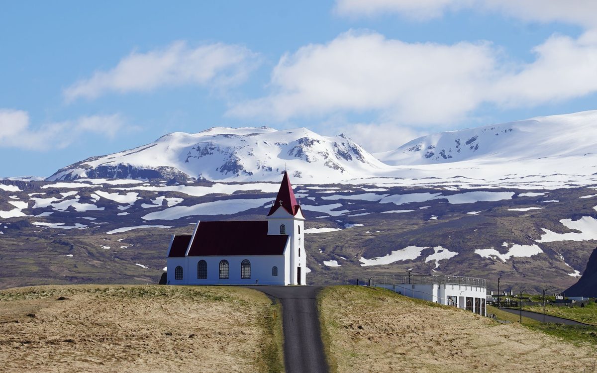 Red-roofed church on a hill below a snow-covered ridge, Iceland